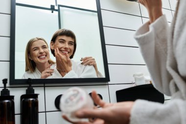 Banyo cüppeli iki kadın otel banyosunda aynanın önünde dikiliyorlar.