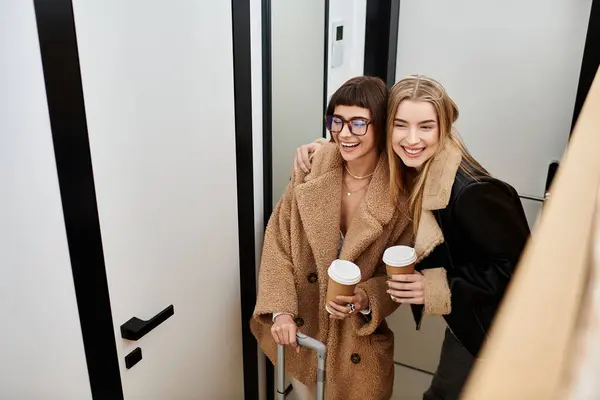 stock image A young lesbian couple stands side by side, exuding style and grace, with luggage in a hotel