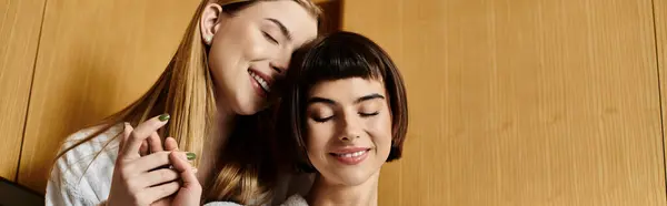 stock image Two young women in bath robes stand next to each other, exuding love and tranquility against a rustic wooden backdrop.