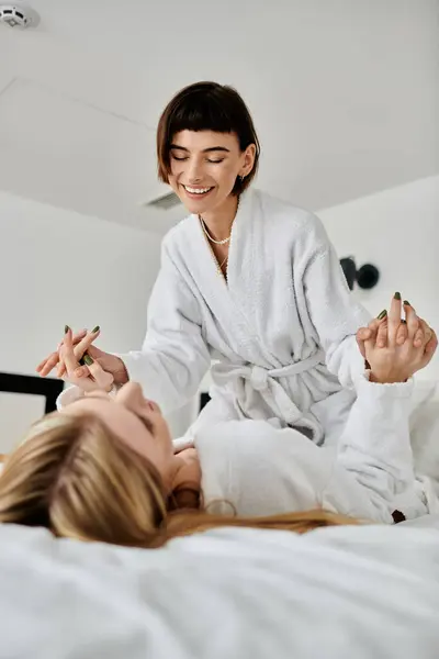 stock image A women in a bathrobe sits comfortably on a bed inside a hotel room, exuding relaxation and intimacy.