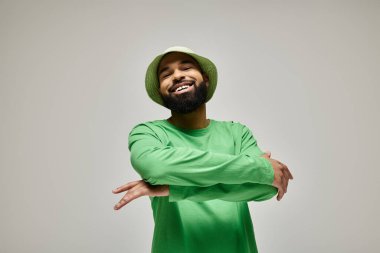 Zarif yeşil şapkalı ve gömlekli yakışıklı Afro-Amerikalı adam canlı arkaplanda poz veriyor..