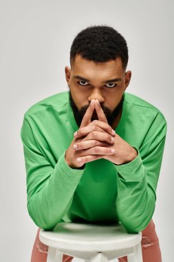 Moda kıyafetli yakışıklı adam beyaz taburede zarifçe oturuyor..