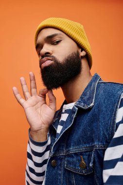 Afro-Amerikalı şık giyinmiş ve sarı şapkalı bir adam, canlı bir arkaplana karşı poz veriyor..