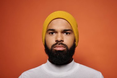 Şık giyinmiş, sarı şapkalı, sakallı yakışıklı Afro-Amerikan bir adam canlı arka planda poz veriyor..