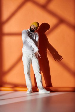 Yakışıklı, şık giyinmiş, turuncu duvarda poz veren bir adam..