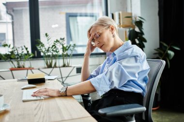 Orta yaşlı, kısa saçlı, ofis ortamında dizüstü bilgisayar kullanan ve menopoz sırasında kendini kötü hisseden bir iş kadını..