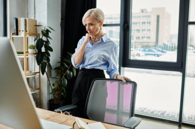 Kısa saçlı orta yaşlı bir iş kadını ofis ortamında çalışırken dizüstü bilgisayarına odaklanır..