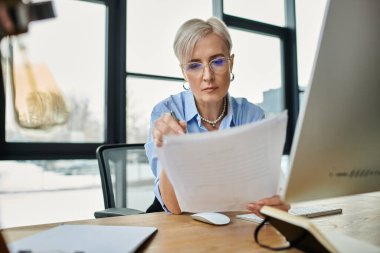 Orta yaşlı, kısa saçlı bir iş kadını laptopuyla ofis ortamında çalışıyor ve verimlilik sergiliyor.