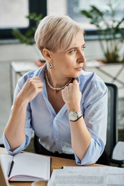 Kısa saçlı orta yaşlı bir iş kadını dizüstü bilgisayarda çalışıyor, menopoz sırasında kendini seksi hissediyor.