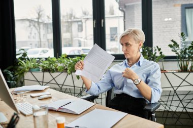 A middle aged businesswoman with short hair seated at a desk, holding a paper, feeling hot during menopause clipart