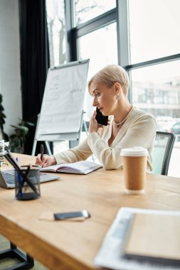 Orta yaşlı iş kadını, kısa saçlı, modern masasında çoklu görev yapan, cep telefonuyla enerjik bir şekilde sohbet eden..