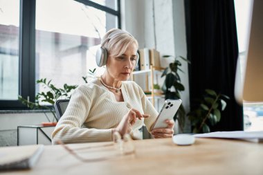 Orta yaşlı iş kadını, kısa saçlı, modern ofis masasındaki tabletine odaklanmış..