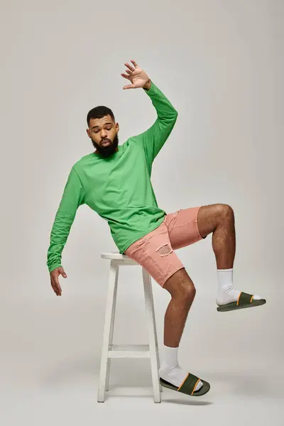 stock image African American man in green shirt and pink shorts posing on vibrant backdrop.