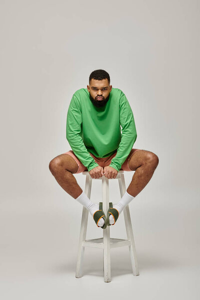 Handsome African American man sitting on stool in stylish green shirt against vibrant backdrop.