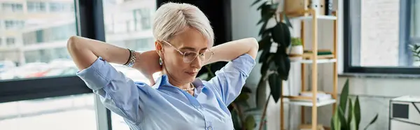 stock image A middle-aged businesswoman with short hair relaxes, her hands behind her head in a gesture of contemplation.