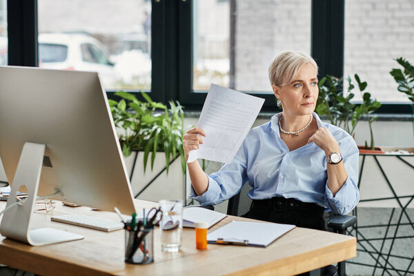 Middle-aged businesswoman with short hair sitting at a desk, deep in thought while holding a piece of paper.