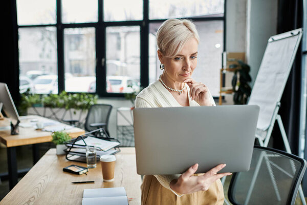 A middle-aged businesswoman with short hair engaging with a laptop in a modern office environment.