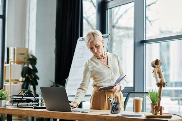 A middle aged businesswoman with short hair standing confidently in front of a laptop computer in a modern office.