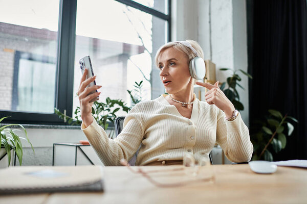 Деловая женщина средних лет с короткими волосами, сидящая за столом, сосредоточенная на своем мобильном телефоне.