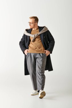 Ceketli ve kazaklı yakışıklı adam elleri ceplerinde güvenle ayakta duruyor..