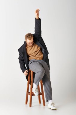 Handsome man in chic attire sitting on top of a wooden stool. clipart