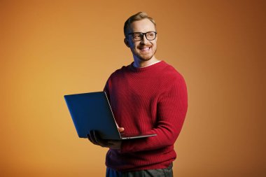 Kırmızı kazaklı yakışıklı bir adam aktif olarak bilgisayarla etkileşime geçiyor..