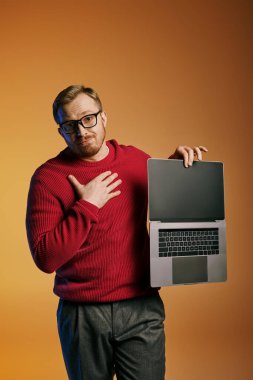 A stylish man in a red sweater confidently holds a laptop. clipart