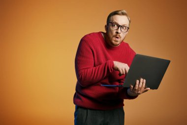 Kırmızı kazaklı şık bir adam aktif olarak dizüstü bilgisayar kullanıyor..