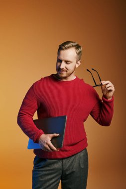 Kırmızı kazaklı yakışıklı bir adam dizüstü bilgisayar tutuyor..