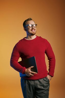 Kırmızı kazaklı şık bir adam dizüstü bilgisayar tutuyor..