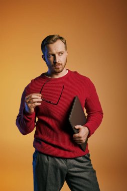 A stylish man in a red sweater actively holding a laptop. clipart