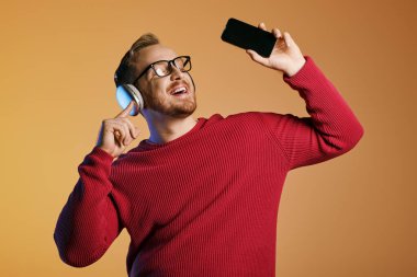 Kırmızı kazaklı şık bir adamın elinde cep telefonu var..