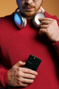 Şık giyinmiş yakışıklı bir adam cep telefonu tutarken kulaklıkla müzik dinliyor..