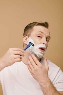 A man in casual attire carefully shaving his face with a razor. clipart