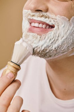 Günlük kıyafetli bir adam nazikçe tıraş kremini fırçayla sürüyor..