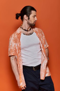 Moda giysileri olan yakışıklı beyaz adam parlak turuncu duvara yaslanıyor..