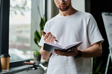 Pencerenin yanında duran, elinde kitap tutan bir adam..