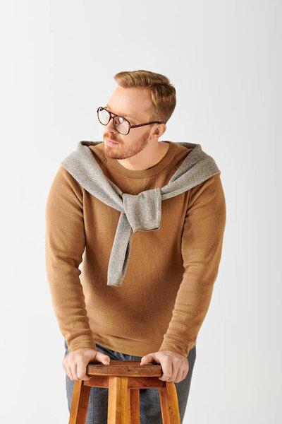 Stylish man in sweater stands confidently on stool.