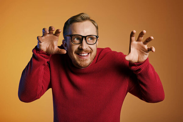 Handsome man in stylish red sweater energetically raises his hands.