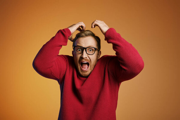 Stylish man in red sweater, holding head in distress.