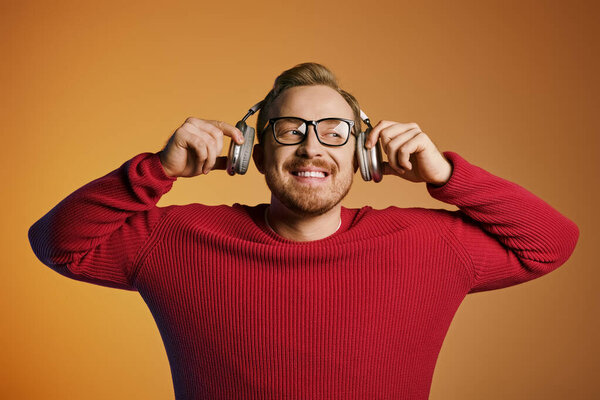 Stylish man in red sweater listening to headphones.