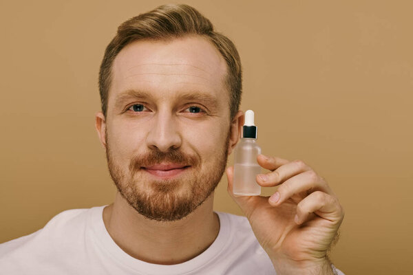 A man in casual attire holds up a small bottle of serum.