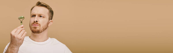 Handsome man in casual attire gently using face roller.