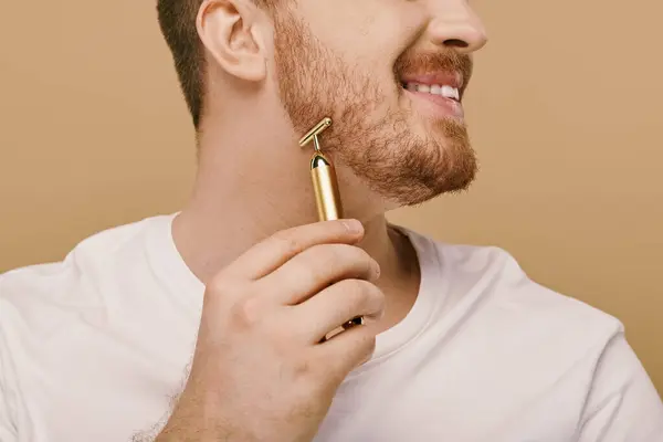 stock image Handsome man in casual attire holds a shiny gold face roller in his hand.