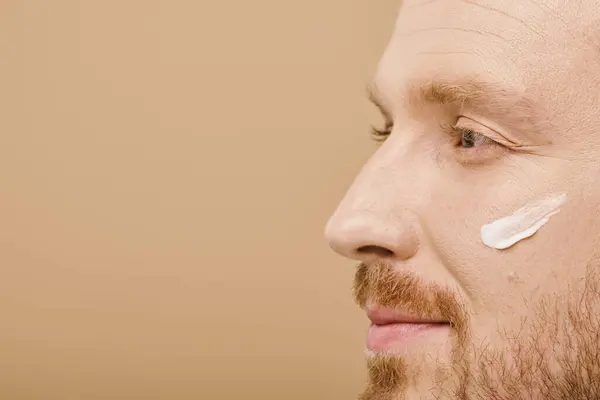 stock image A handsome man in casual attire applying cream to his face.