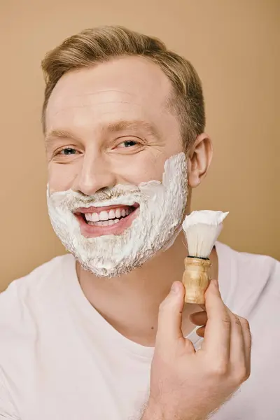 stock image A man in casual attire applying shaving cream with a brush.