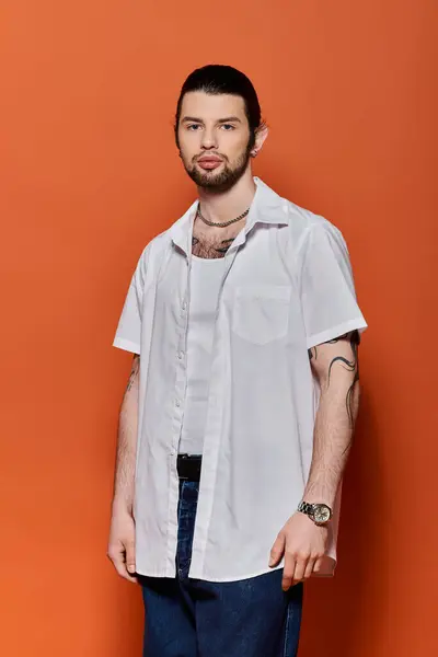 stock image A handsome Caucasian man in trendy attire standing confidently in front of an orange wall.