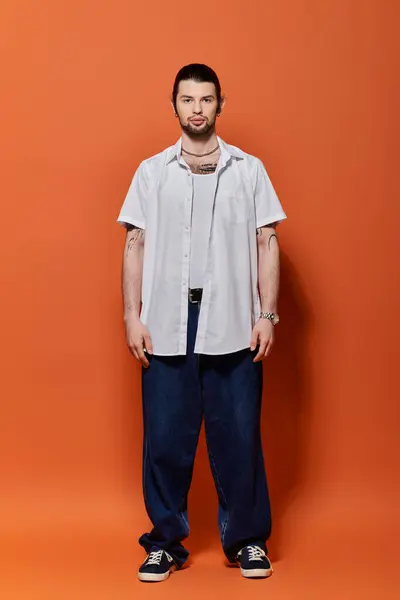 stock image A stylish Caucasian man standing confidently in front of a bright orange wall.