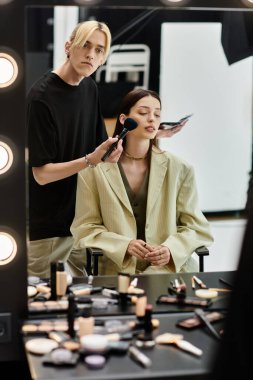 Woman sits at mirror, getting makeup done by artist. clipart