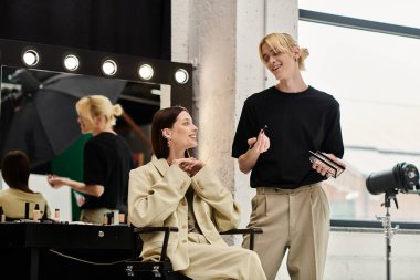 Makyaj sanatçısı aynanın önünde makyaj yaparken kadın sandalyede oturuyor..